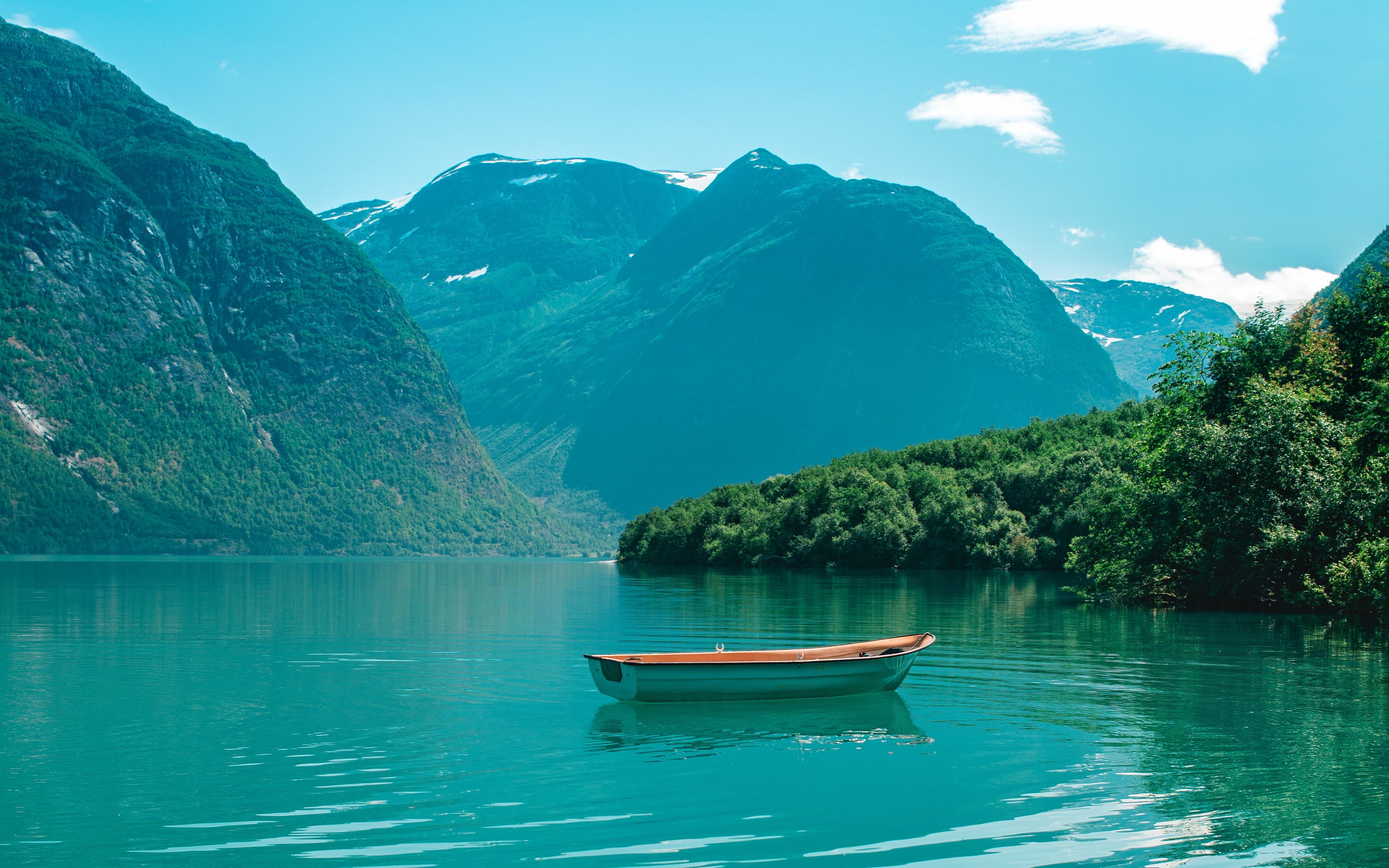A small wooden rowboat floating on a calm turquoise lake surrounded by lush green mountains and forests under a clear blue sky
